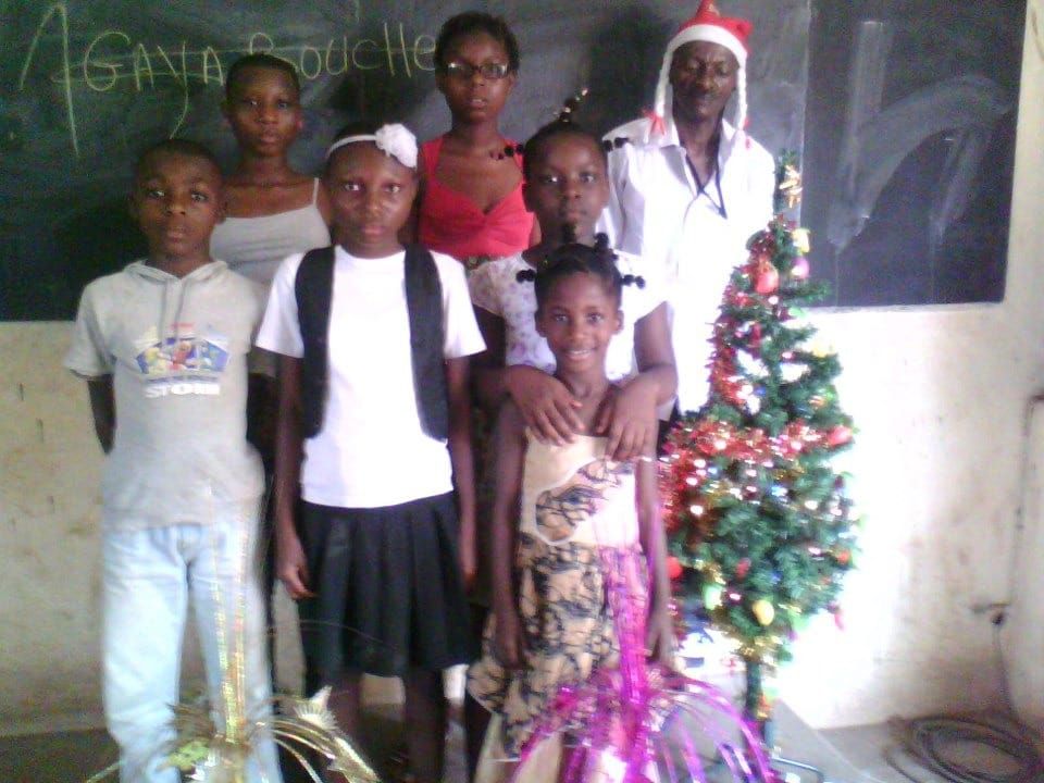 Children standing with a volunteer next to a small Christmas tree in a classroom