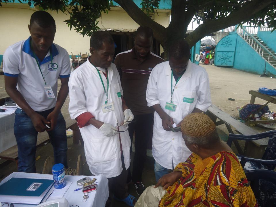 Volunteer medics in white coats checking a patient's results under a tree